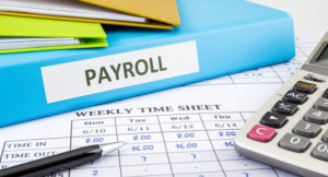 PAYROLL word on blue binder place on weekly time sheet and payroll summary report, human resources concept
